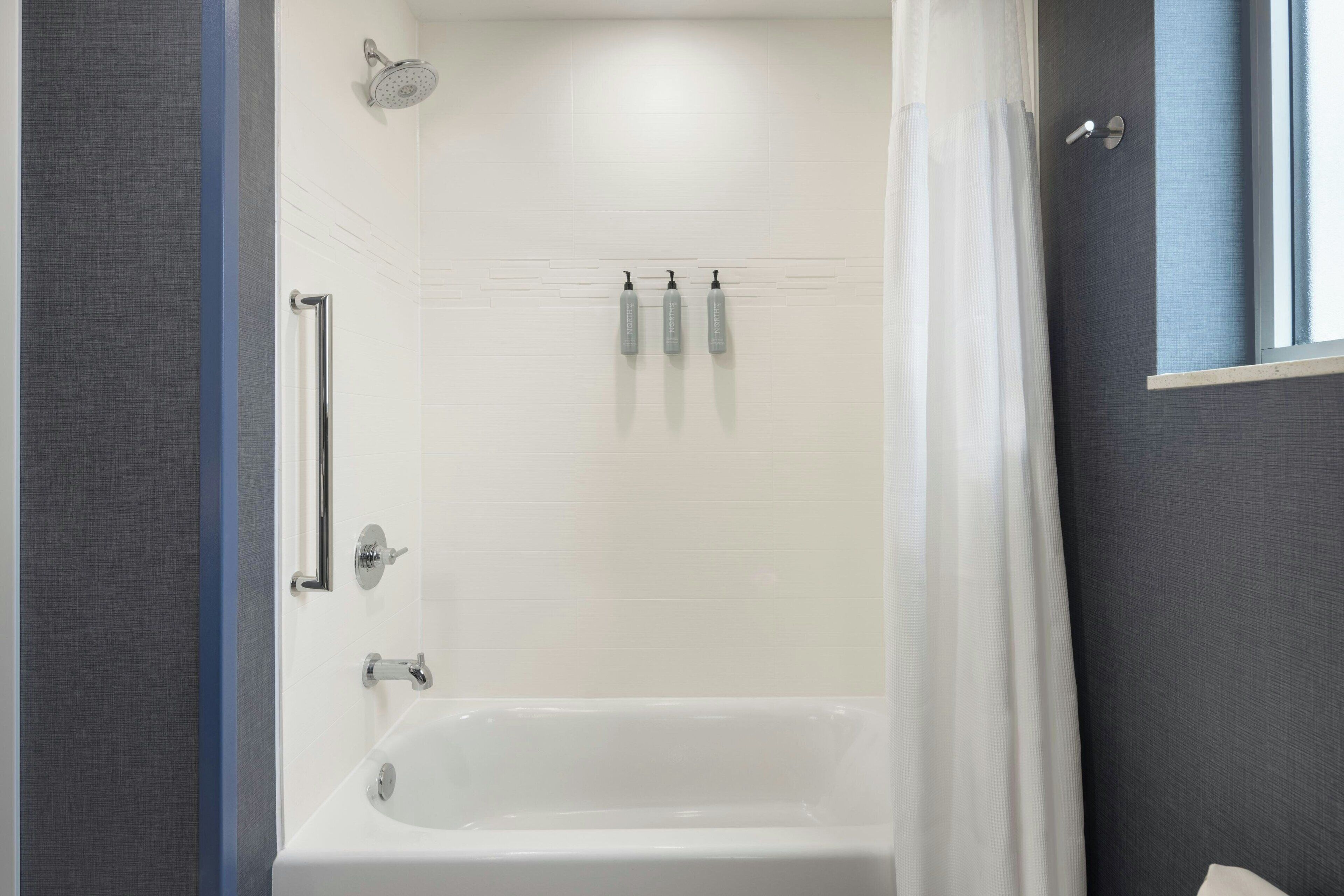 Ein modernes Badezimmer mit Badewanne, Duschkopf und drei Flaschen Shampoo und Conditioner an der Wand.