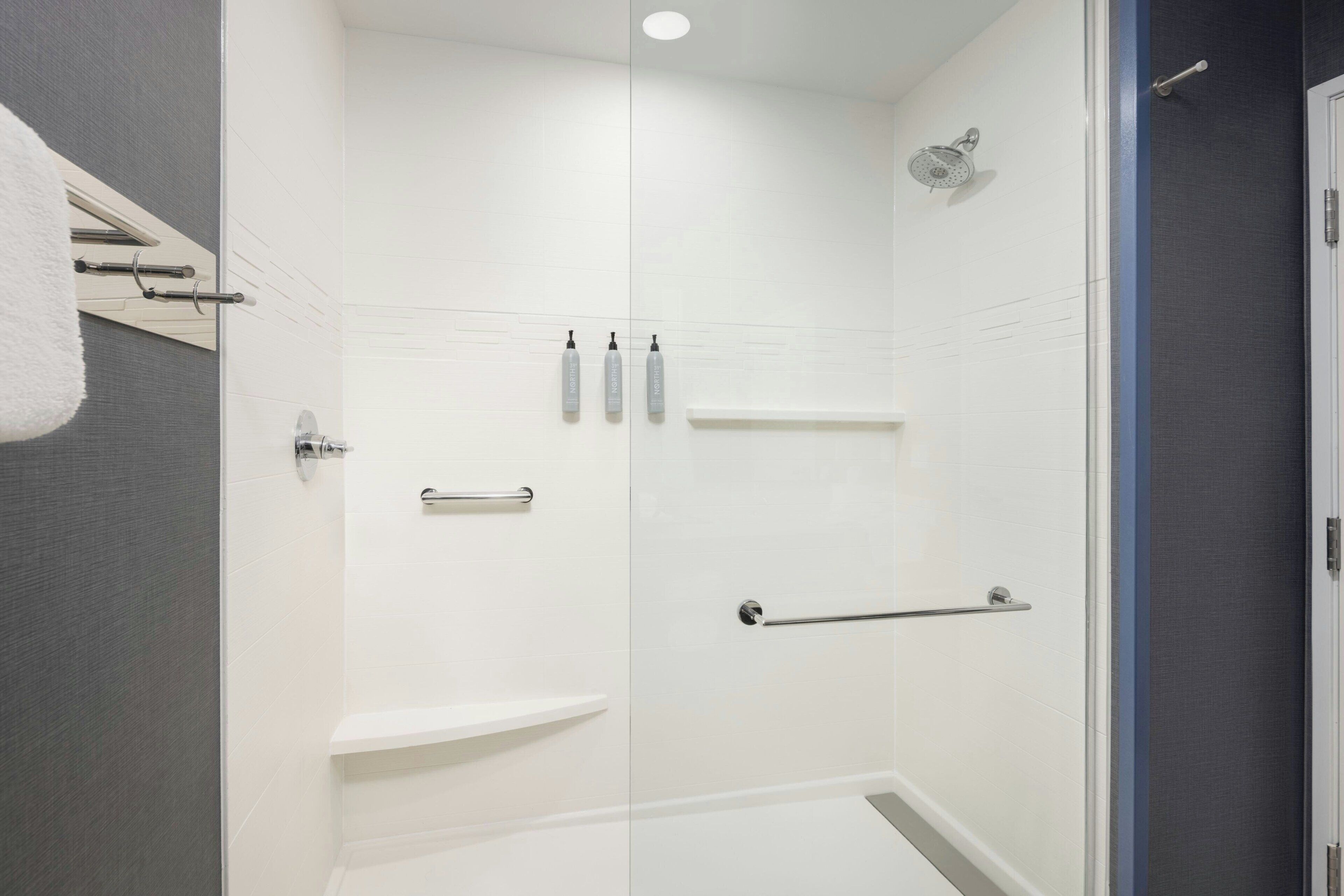 A modern bathroom with a glass shower enclosure, white tiles, and a towel rack.