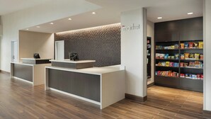 A modern reception desk with a 'market' sign, a patterned wall, and a snack shelf. - Residence Inn by Marriott Battle Creek (Battle Creek)
