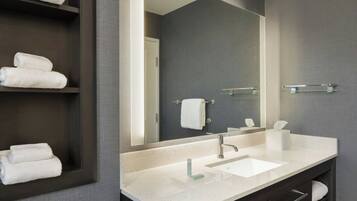 Un baño moderno con un espejo grande, tocador de madera oscura, lavamanos blanco y varias toallas en estantes.
