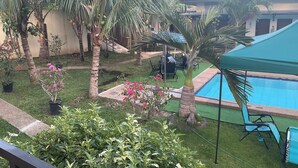 Un espace piscine agrémenté de palmiers, un coin salon abrité et un petit jardin parsemé de fleurs roses.