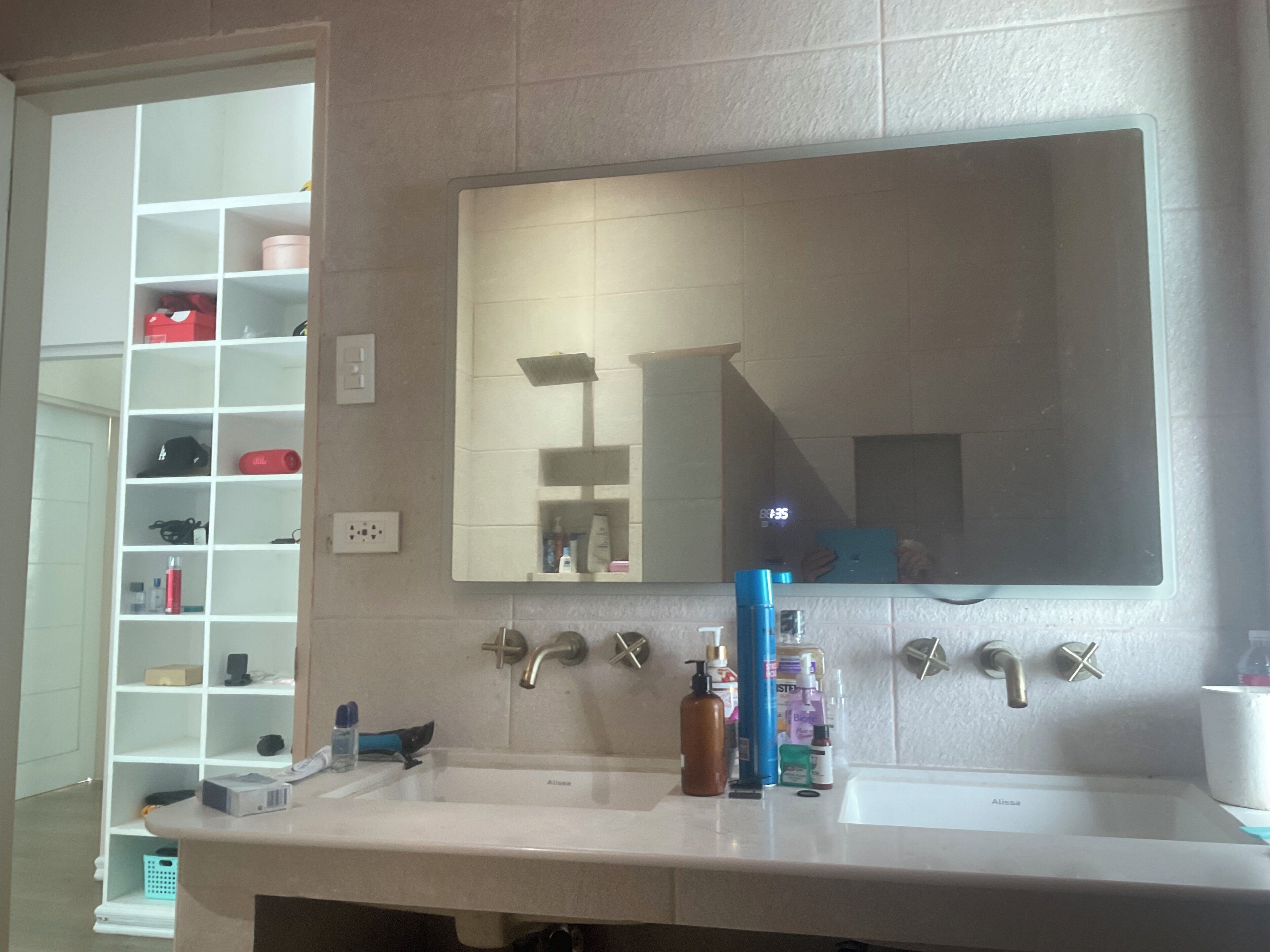 A bathroom with a double sink, a large mirror, and a storage unit with shelves.