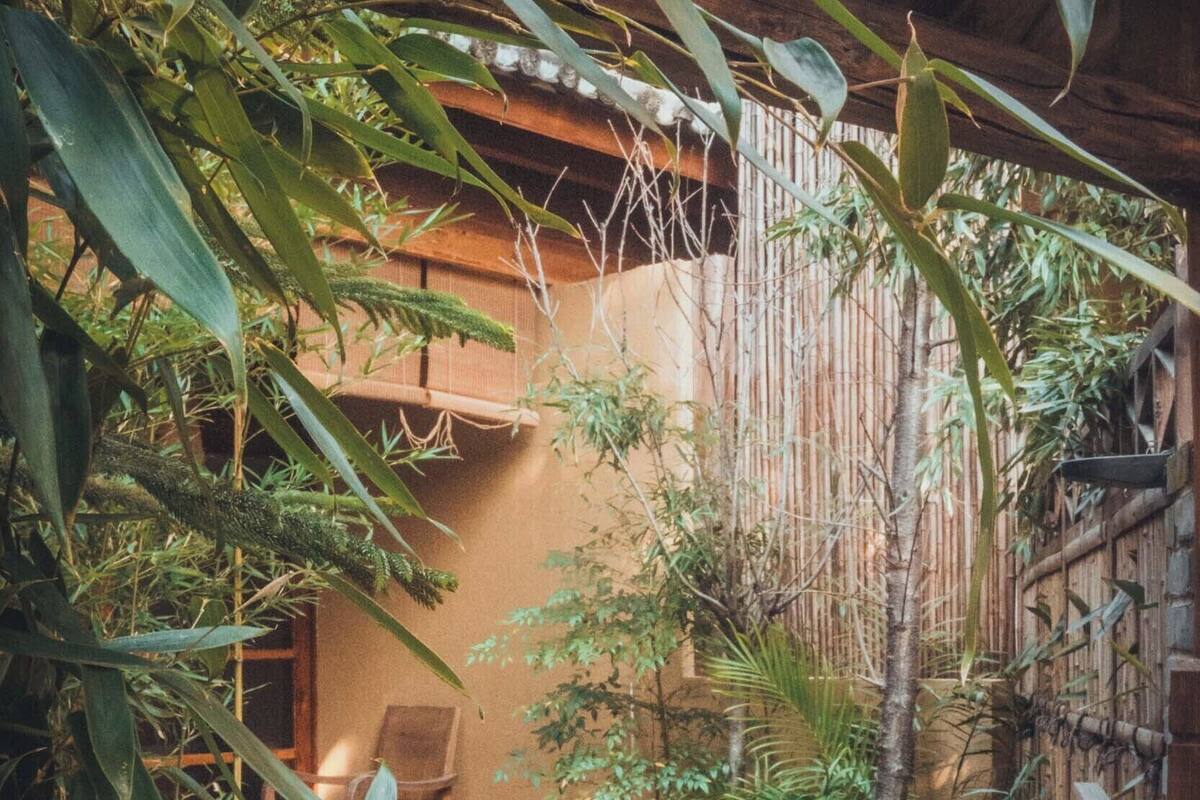 A wooden deck with a chair, surrounded by dense foliage and bamboo structures.