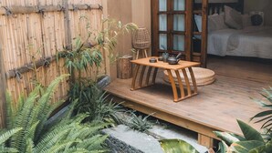 A wooden deck with a table and chairs, bamboo wall, and various plants.