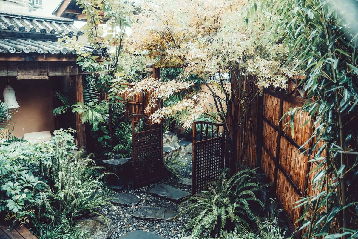 A traditional Japanese garden with a wooden gate, stone pathway, and various plants.