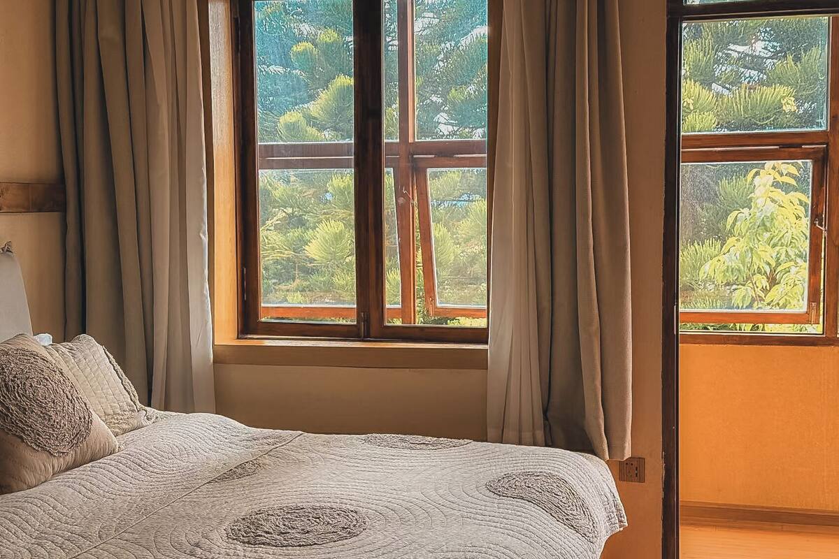 A bedroom with a large window, a bed with a quilt, and curtains.