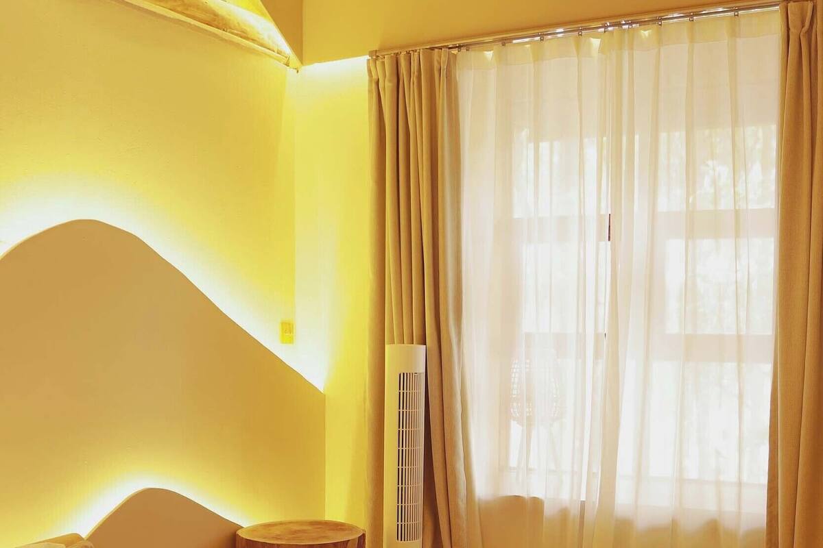 A room with a bed, a small round table, and a large window with curtains.