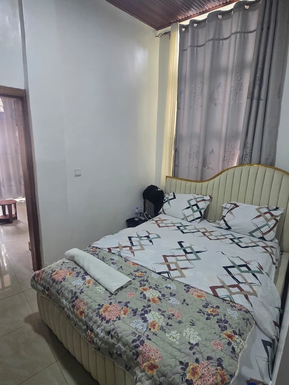 Une chambre à coucher avec un lit, une table de chevet, une chaise et une fenêtre avec des rideaux.