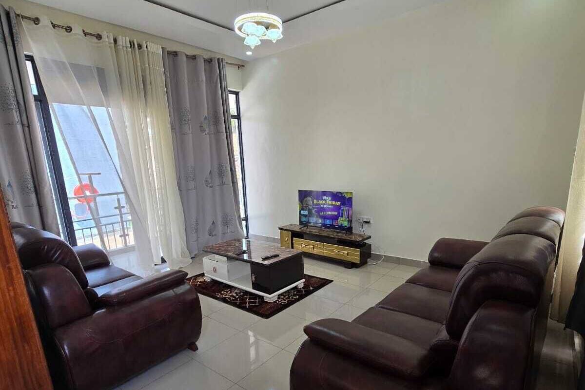 A modern living room with leather sofas, a flat-screen TV, and a chandelier.