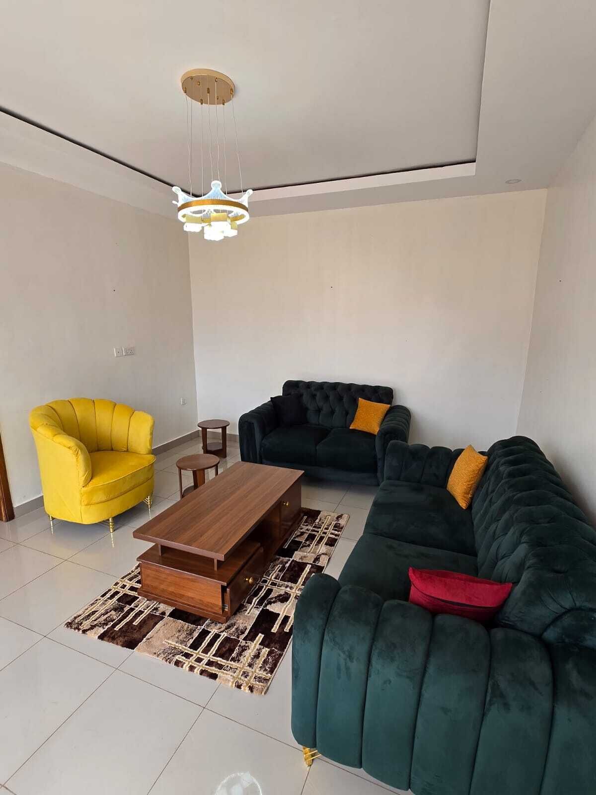 A modern living room with a yellow armchair, a dark green sofa with yellow and red cushions, a wooden coffee table, and a patterned rug.