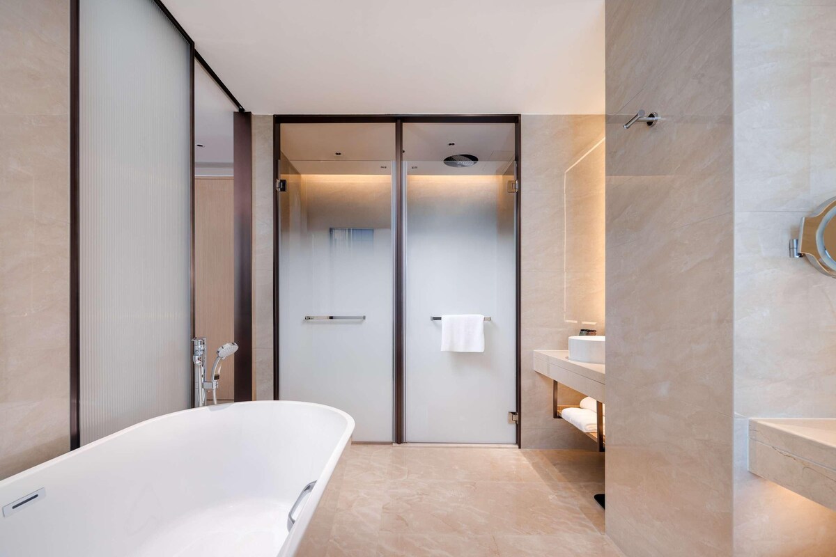 Een moderne badkamer met een vrijstaand bad, een douchecabine met glazen wanden en een wastafel met spiegel.