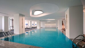 Una piscina interior moderna con agua cristalina, rodeada de paredes blancas y un techo con iluminación empotrada.