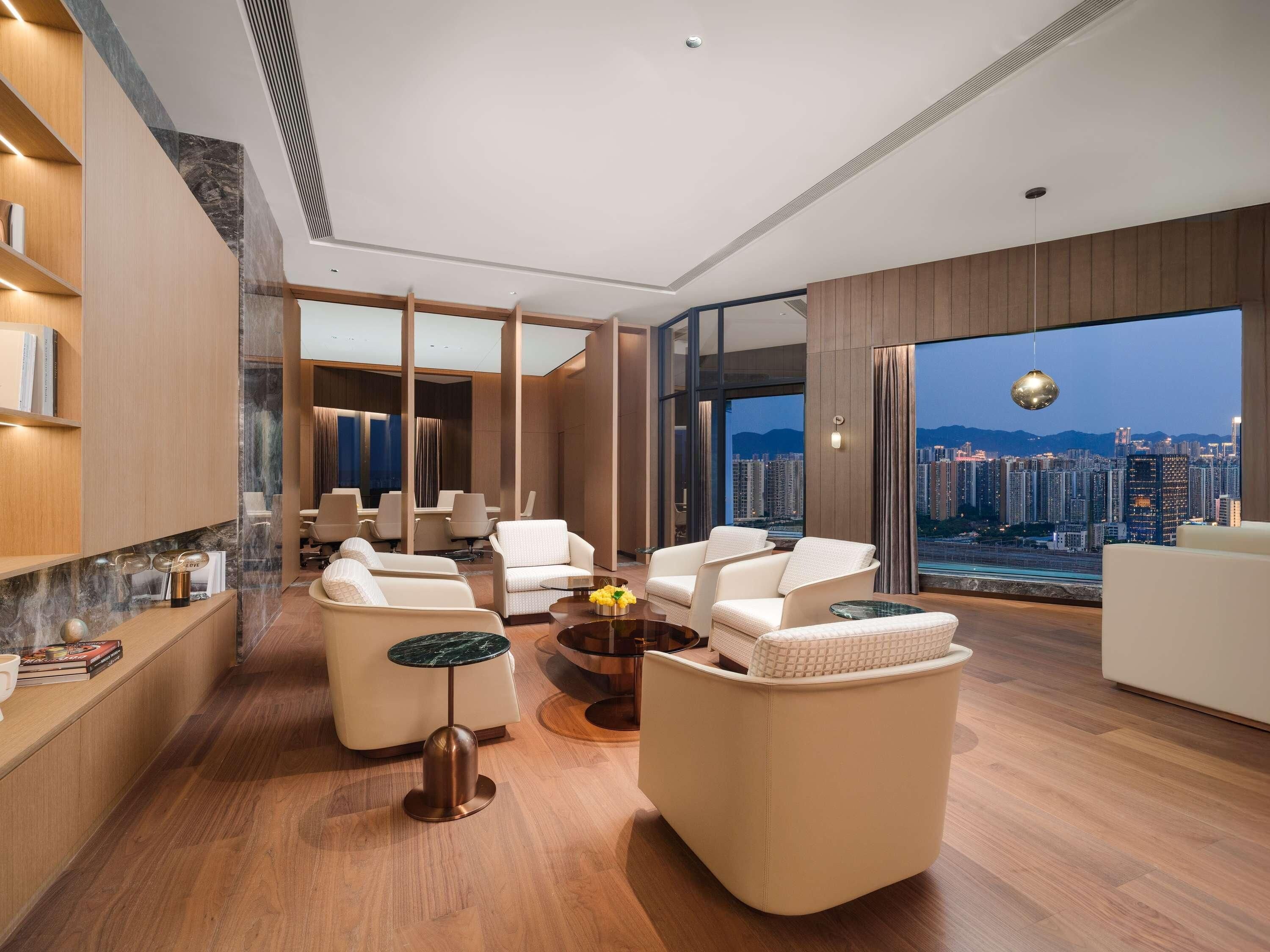 Uma sala de estar moderna com vista para a cidade, com um sofá, poltronas, uma mesa de centro e uma estante.