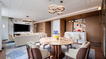 Quarto de hotel moderno com uma mesa de jantar redonda de mármore, assentos confortáveis, uma TV de tela plana e uma parede decorativa com prateleiras.