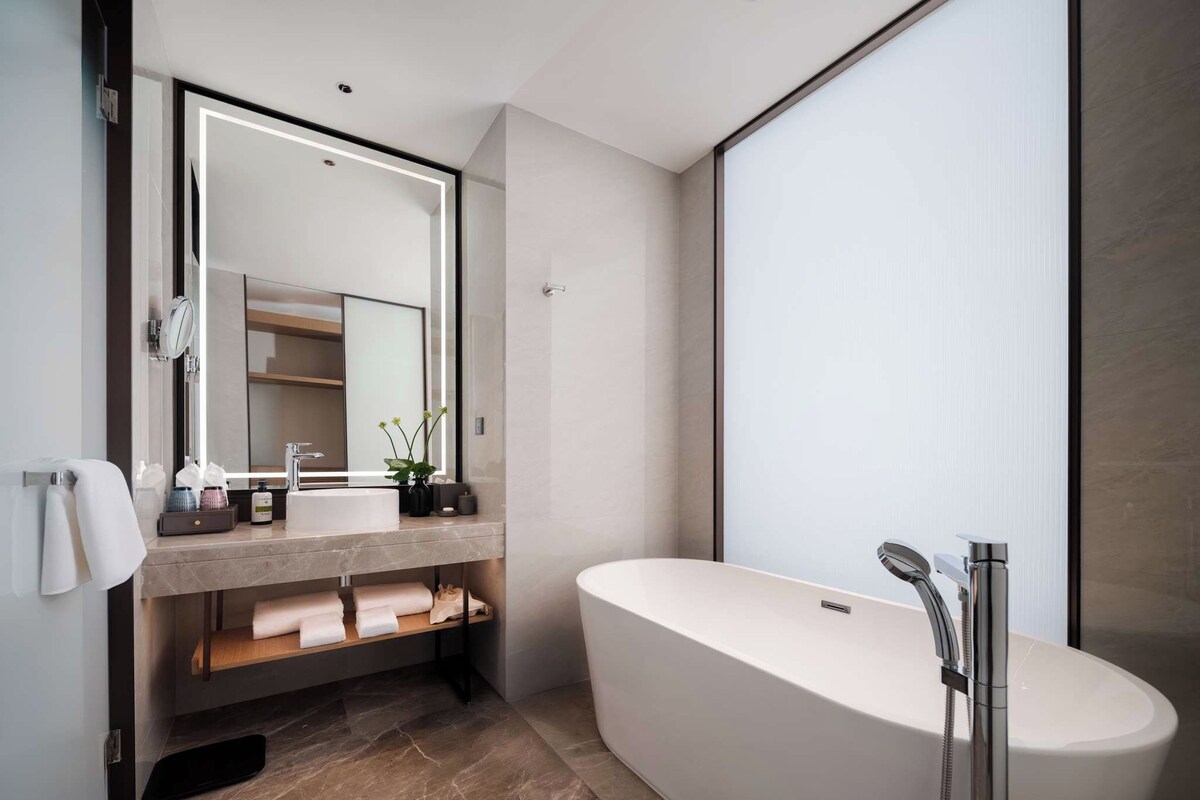 A modern bathroom with a freestanding bathtub, a large mirror, and a vanity with a sink and towel rack.