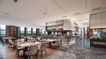 Um restaurante espaçoso com pé-direito alto, um bar central e vista para a cidade.
