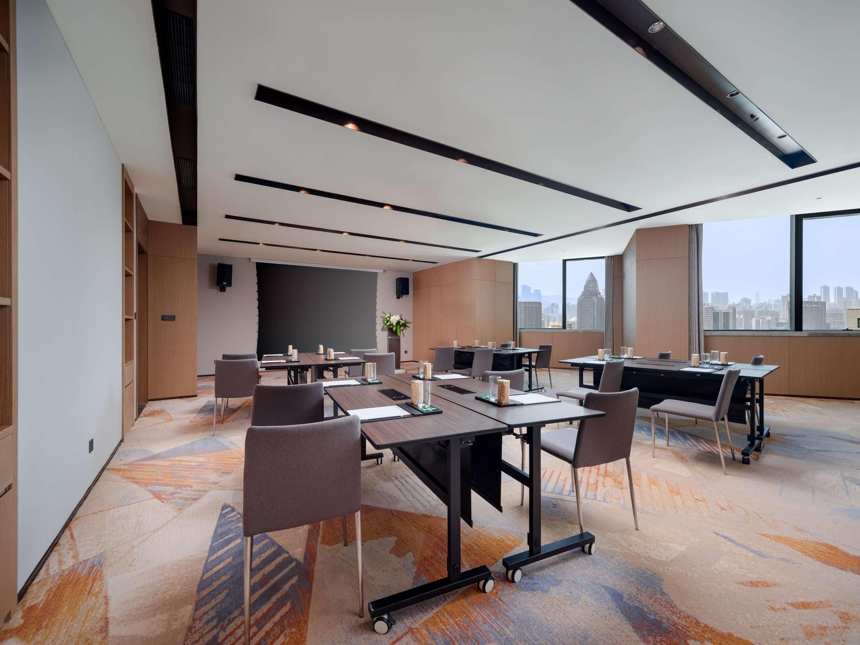 A modern conference room with multiple tables, chairs, and a large window offering a city view.