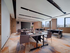 Una sala de conferencias moderna con varias mesas, sillas y un ventanal que ofrece vistas a la ciudad.