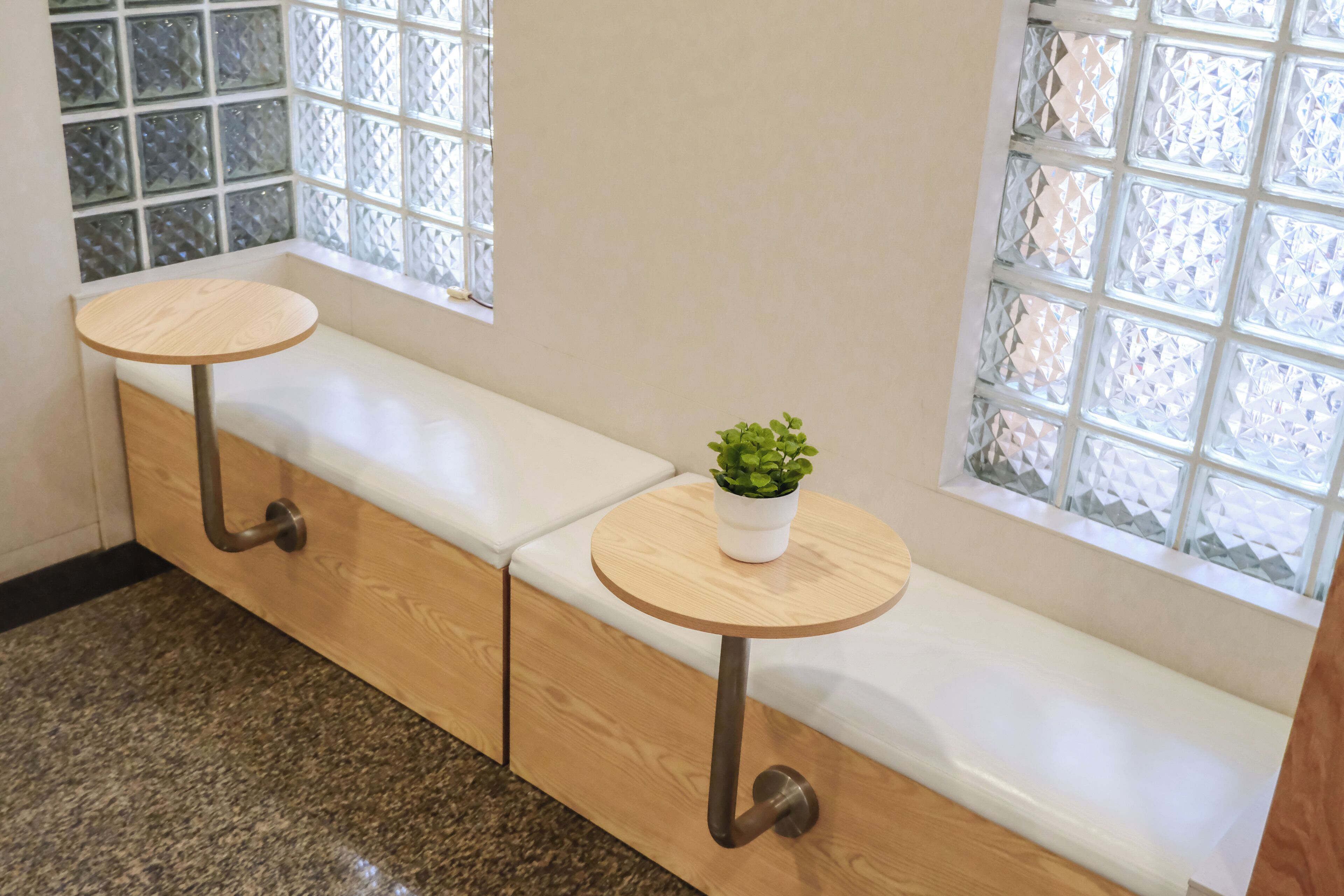 A seating area with two round tables and a bench, a potted plant on one table, and a window with a geometric pattern.