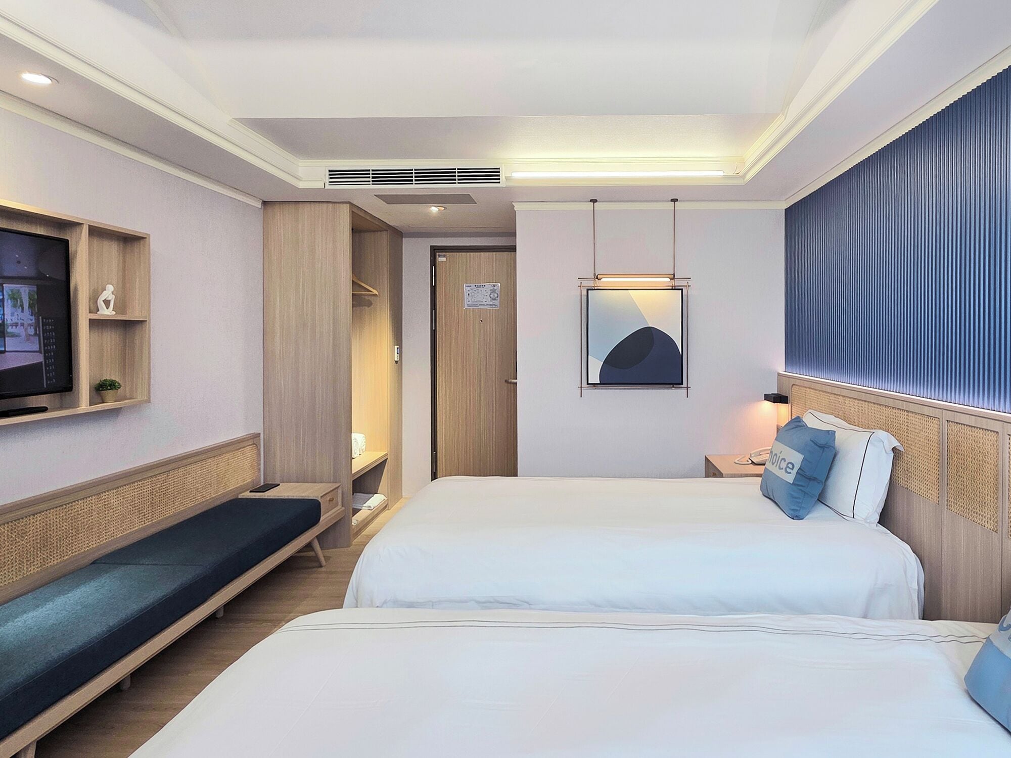 A hotel room with two beds, a TV, a bedside table, a lamp, and a wardrobe.