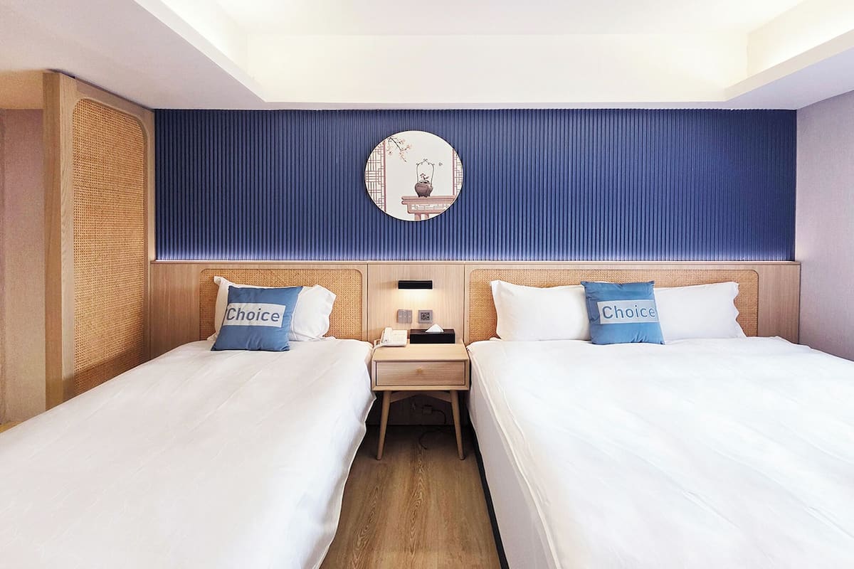 Habitación de hotel con dos camas, una mesita de noche, un reloj y un espejo colgado en la pared.