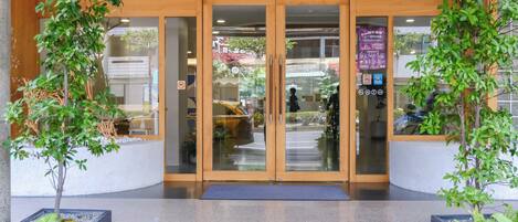 A hotel entrance with a glass door, a wooden ceiling, and potted plants.