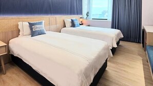 Hotellihuone, jossa on kaksi sänkyä, ikkuna, jossa on verhot, yöpöytä ja näkymä kaupunkiin.
