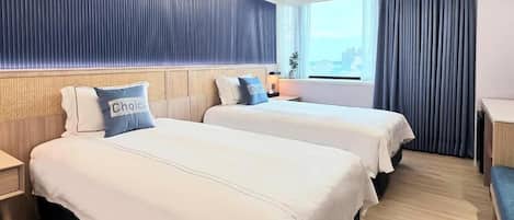 Habitación de hotel con dos camas, una ventana con cortinas, una mesita de noche y vista a la ciudad.