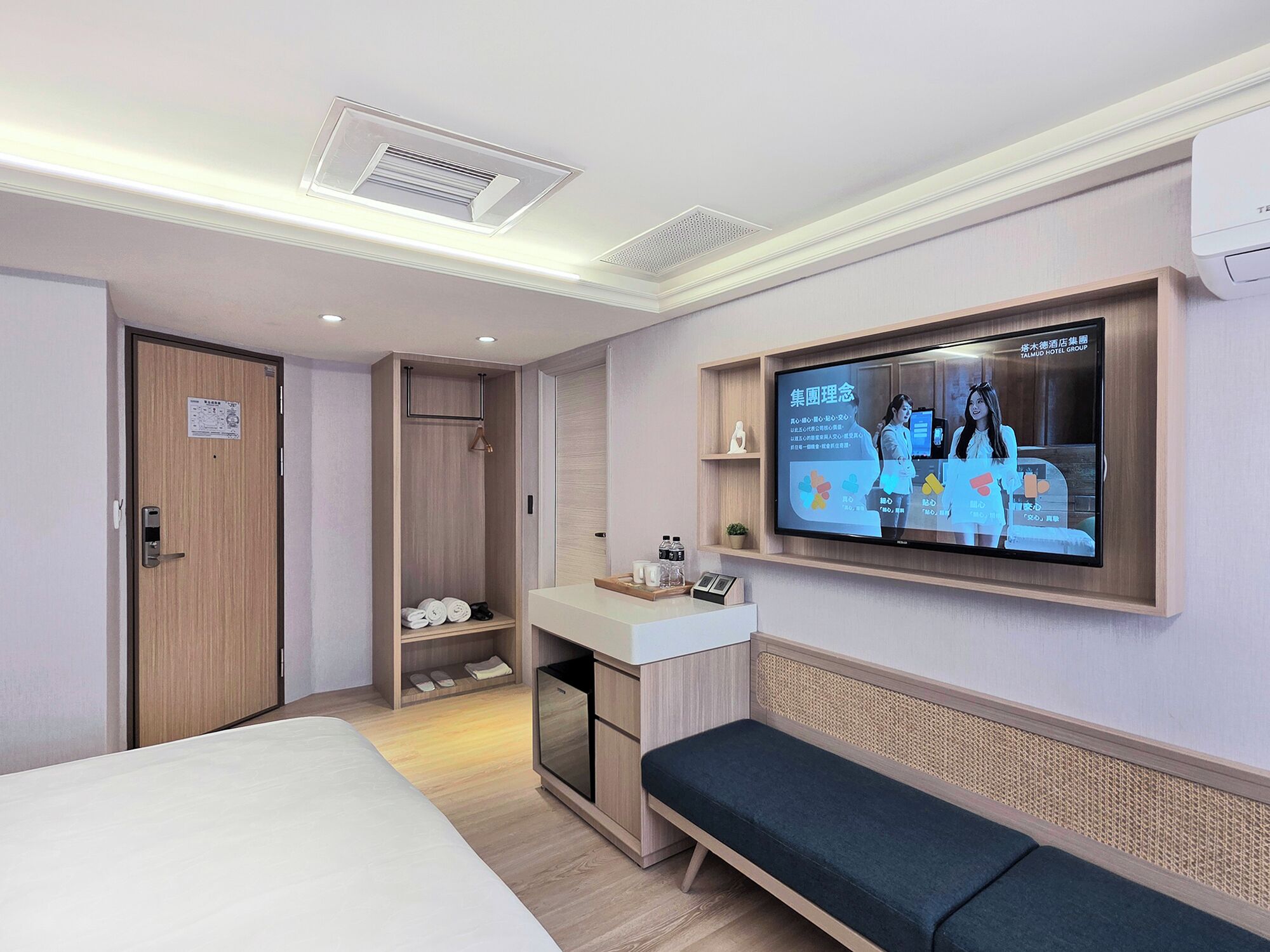 A modern hotel room with a bed, a seating area, a TV, and a small kitchenette.
