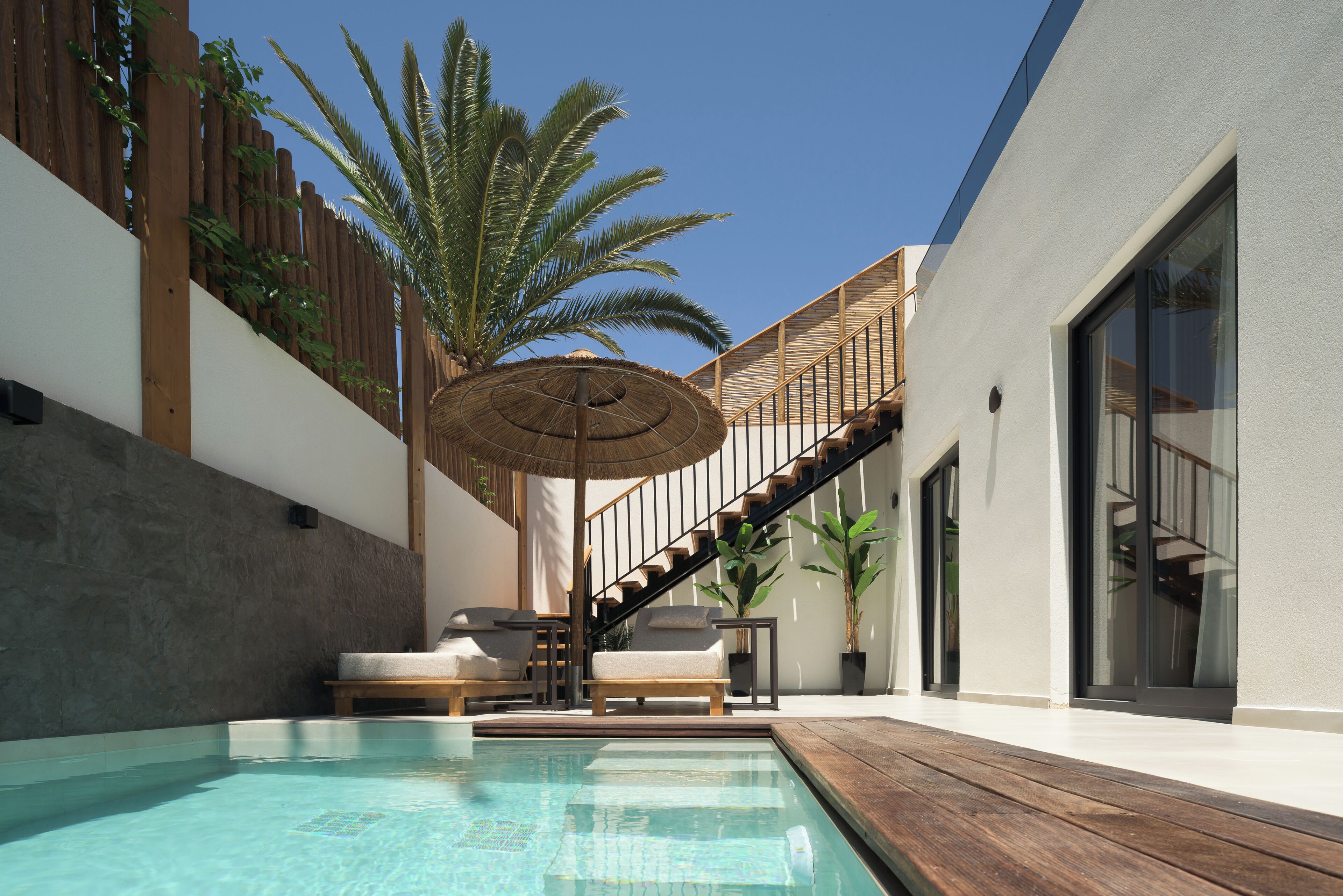 Una piscina con lettini, un solarium in legno, una scala e un ombrellone grande.