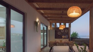 Een moderne eethoek met een glazen wand, houten plafond en uitzicht op zee.