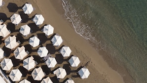 Een luchtbeeld van een strand met rijen witte parasols en strandstoelen.
