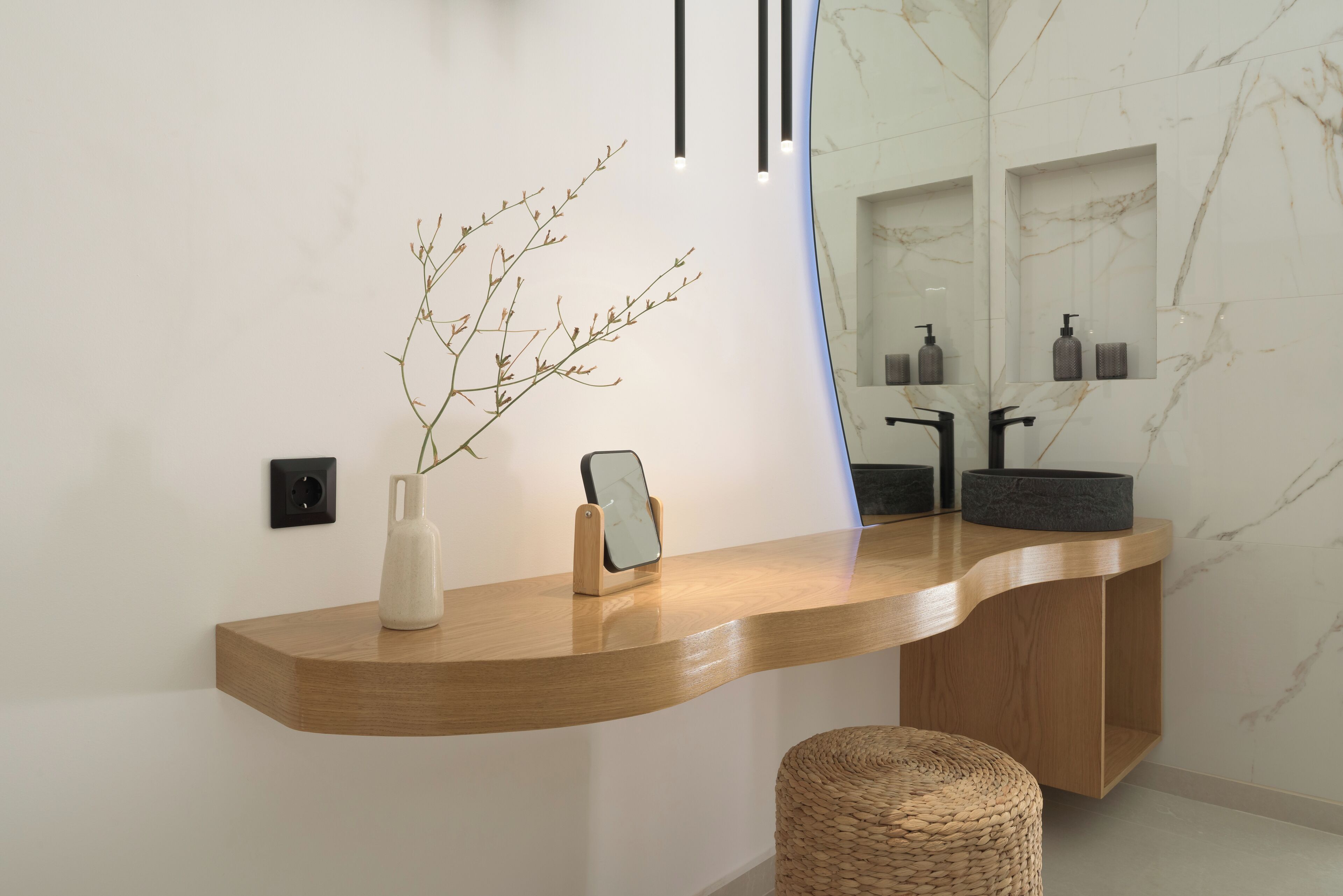Een moderne badkamer met een houten wastafelmeubel, een spiegel, een wastafel en een decoratieve tak.