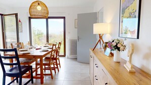 A dining area with a wooden table and chairs, a hanging light fixture, a radiator, and a view through a glass door.