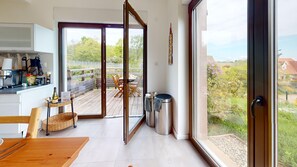 A modern kitchen with a dining area, large sliding glass doors to a deck, and a view of a garden and buildings. - Gite du Holzweg Les Cigognes Duplex (Mittelbergheim)
