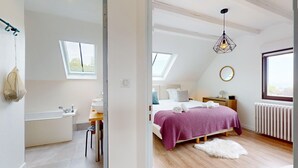 A modern bedroom with a skylight, a bed with a purple blanket, a wooden dresser, and a white radiator.