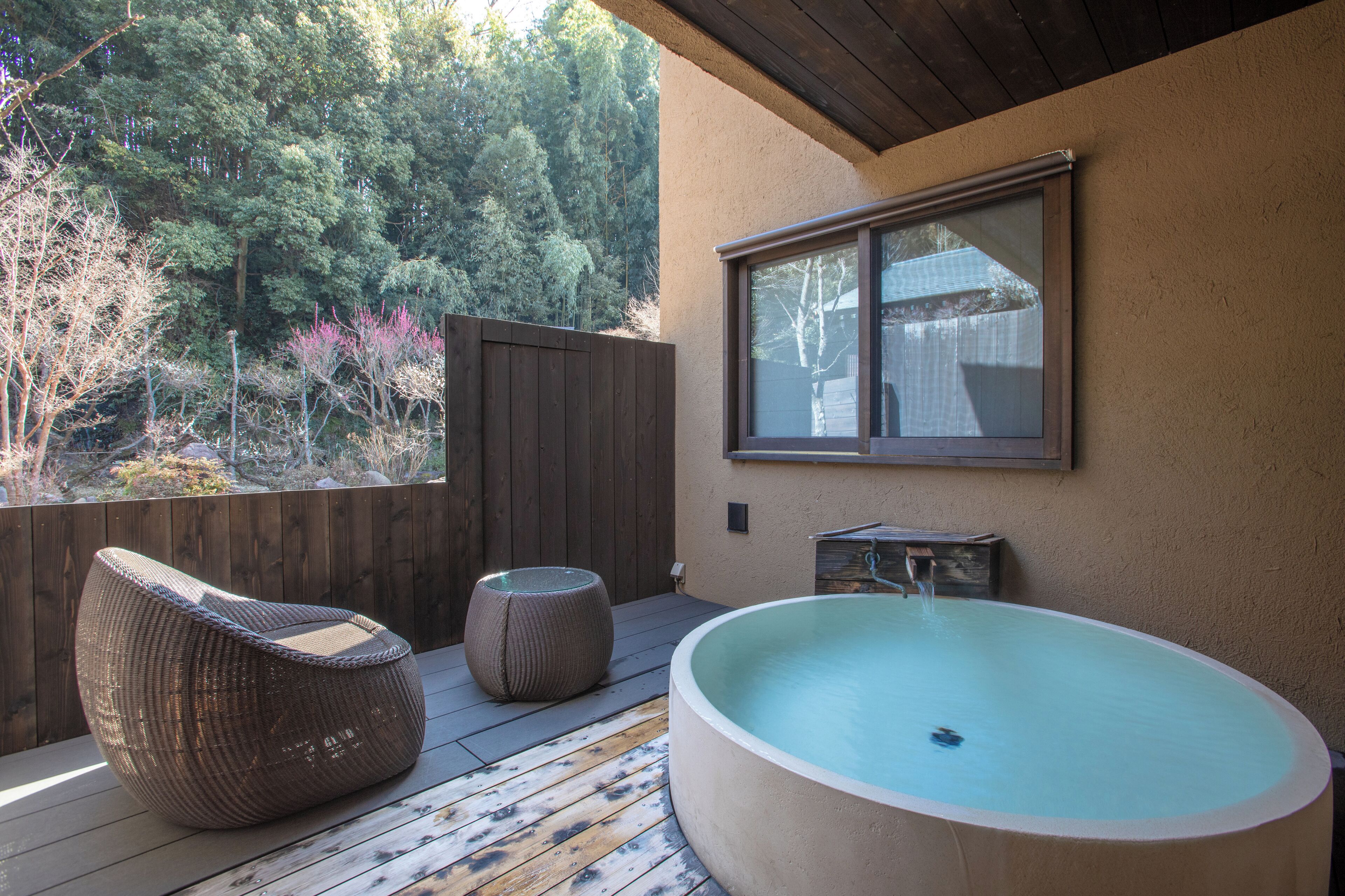 A wooden deck with a large hot tub, a wicker chair, and a small table.