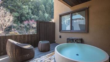 A wooden deck with a large hot tub, a wicker chair, and a small table.
