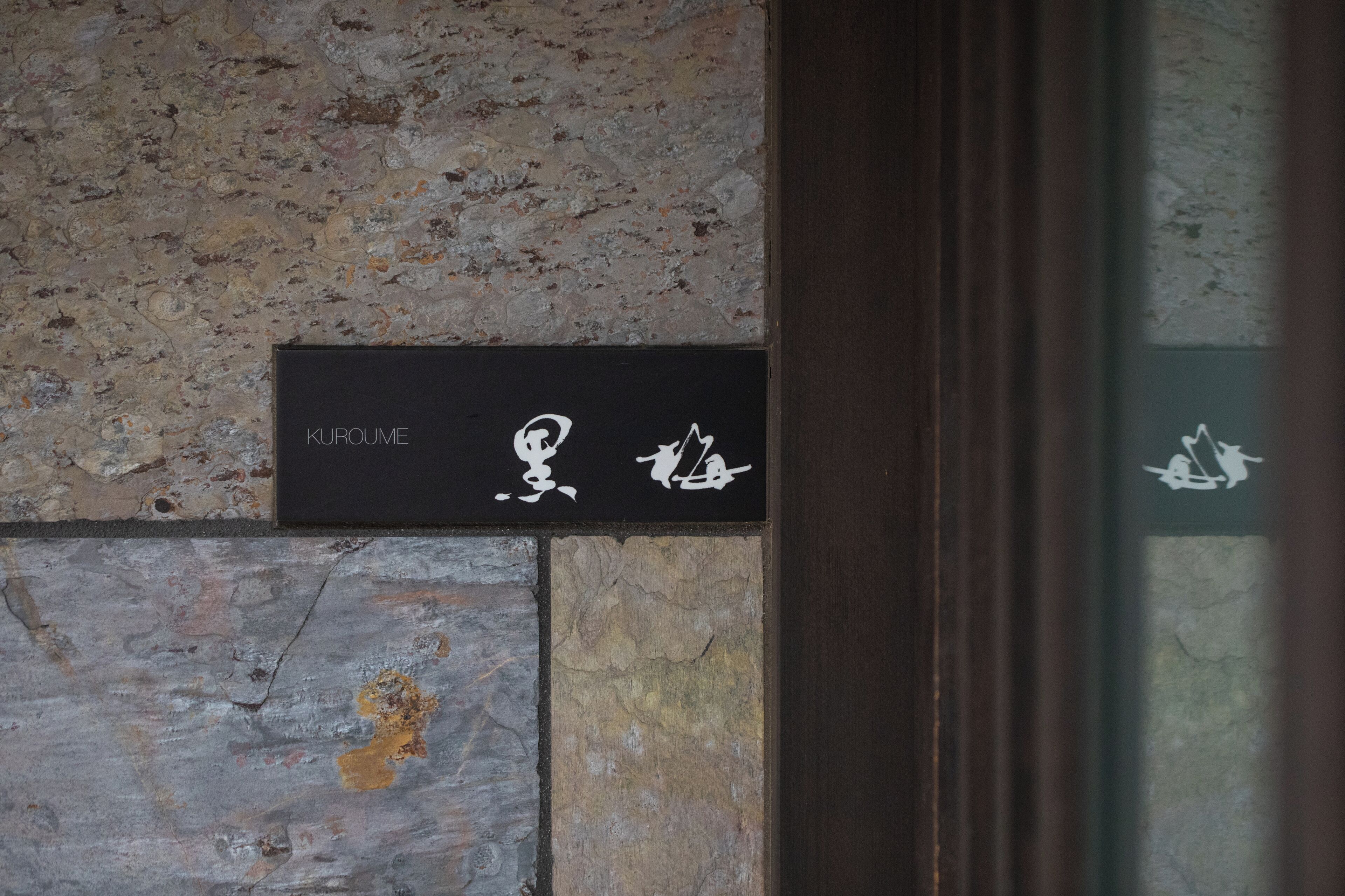 A black sign with white text and symbols on a stone wall.