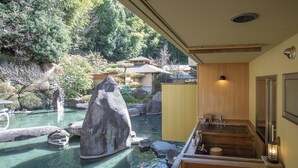 Een traditioneel Japans onsen met een houten badgedeelte, een stenen rots en koi karpers in het water.