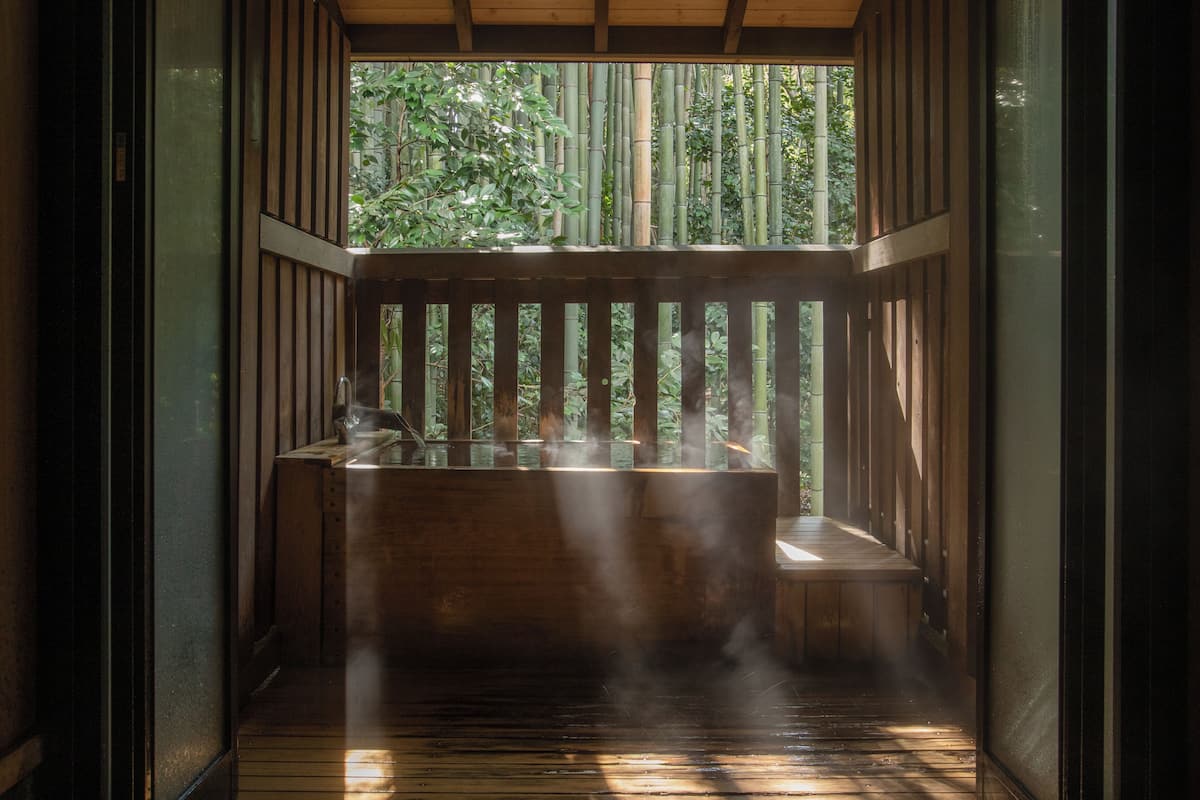 Ein traditioneller japanischer Raum mit Holzboden, einer Sitzgelegenheit auf Tatami-Matten und Blick auf Bambus.
