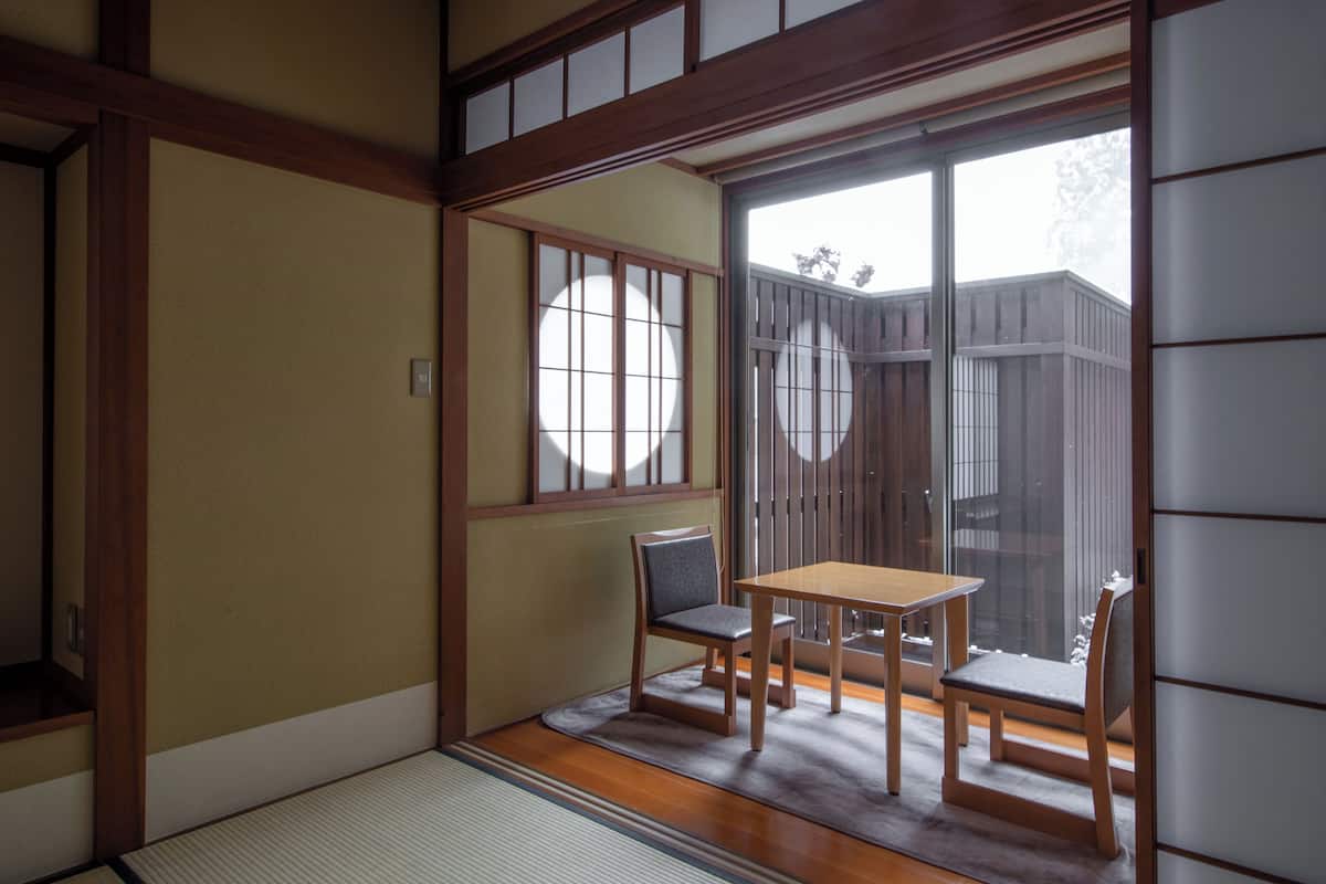 Ein traditioneller japanischer Raum mit Tatami-Böden, einer Schiebetür und einem Holztisch mit Stühlen.