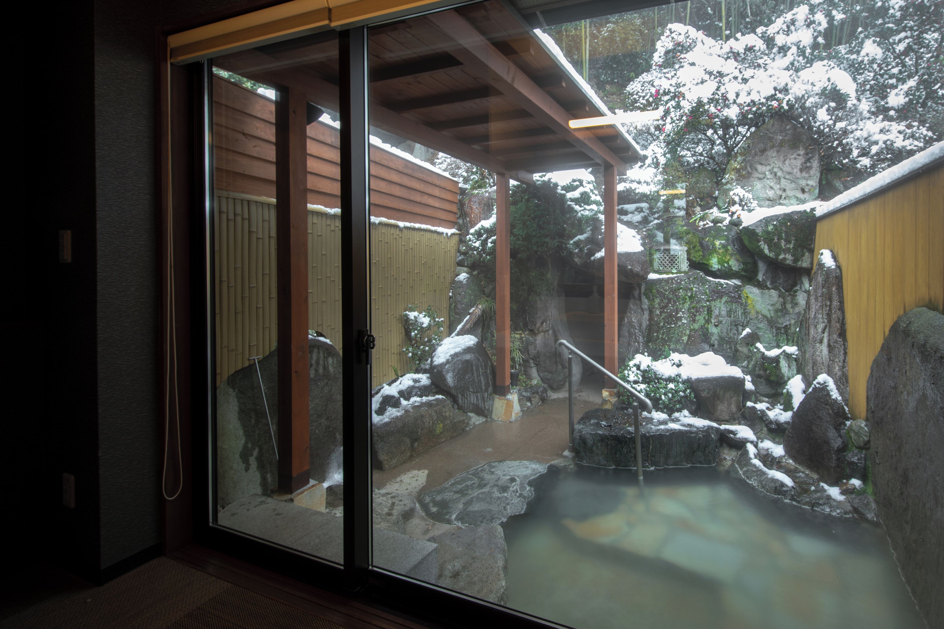 Ein traditioneller japanischer Garten mit Thermalbad, Holzbauten und schneebedeckten Felsen.