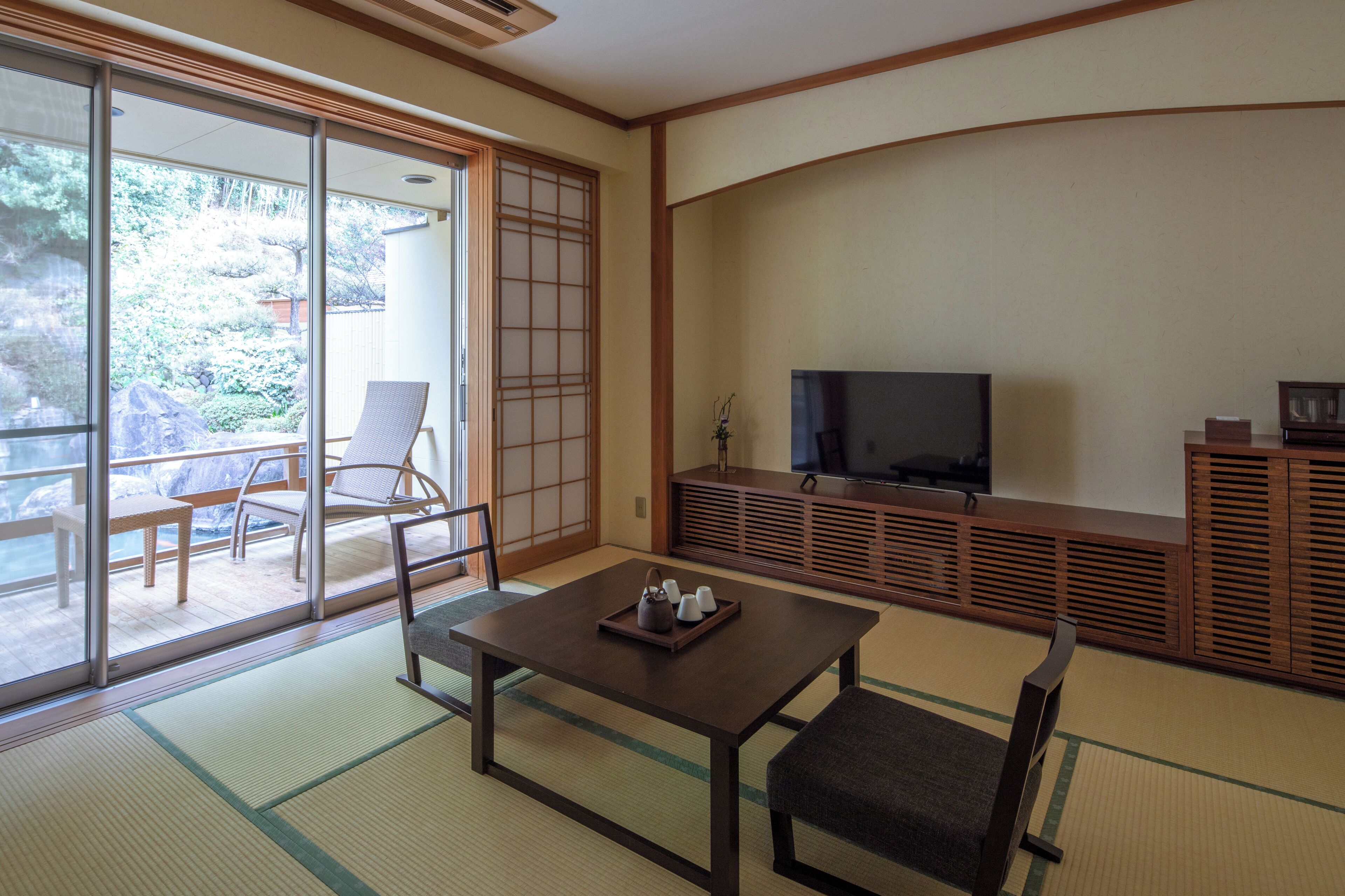 A traditional Japanese room with tatami flooring, a low table with a tray, a television, and a sliding door leading to a balcony.