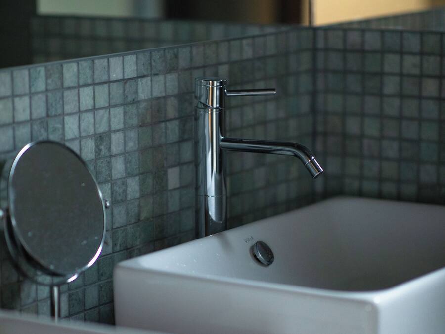 A bathroom with a white sink, a mirror, and a chrome faucet.