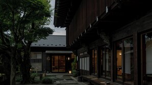 Een traditioneel Japans gebouw met een grindhof, houten banken en een grote boom.