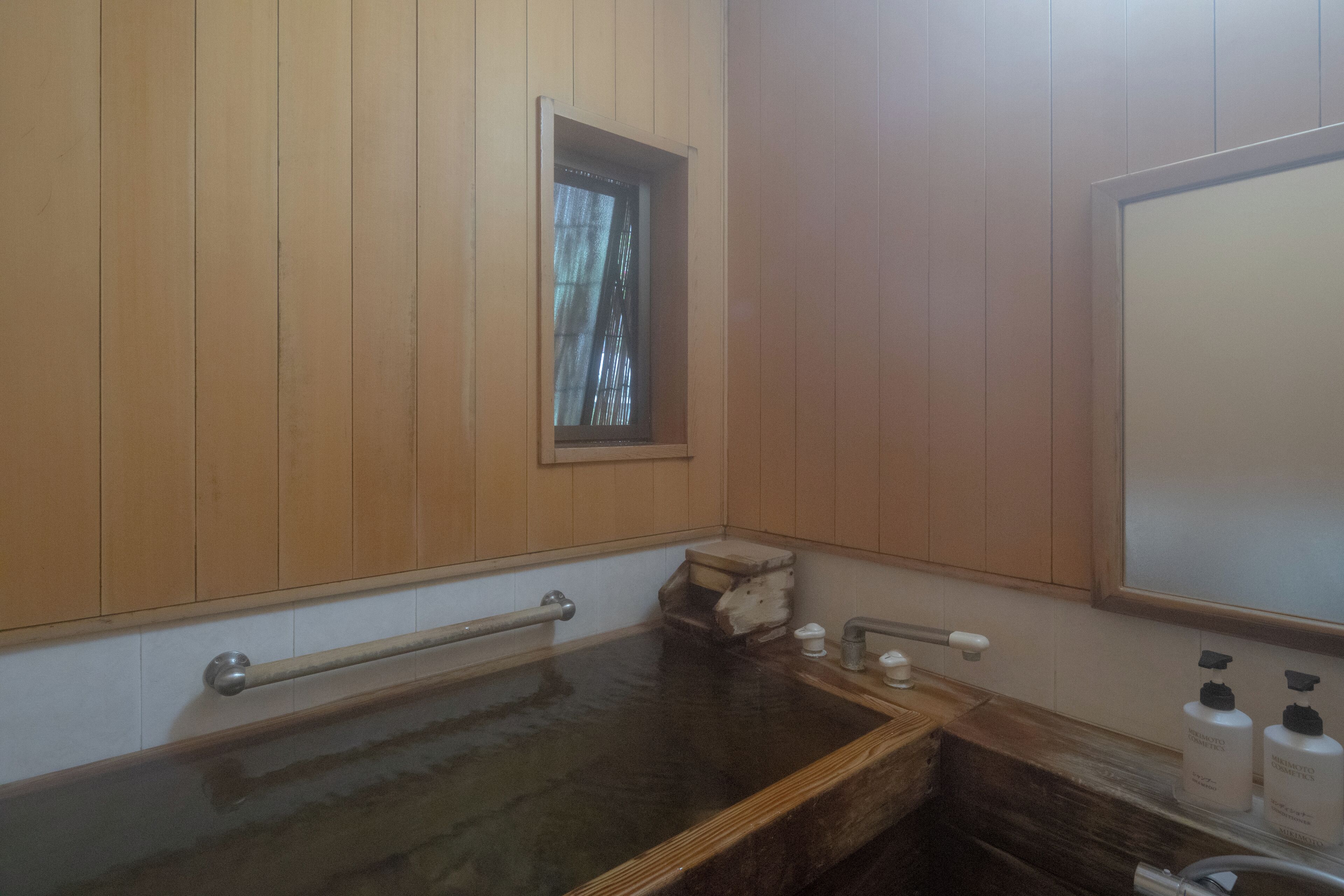 A wooden-paneled room with a wooden bathtub, a window, and a mirror.