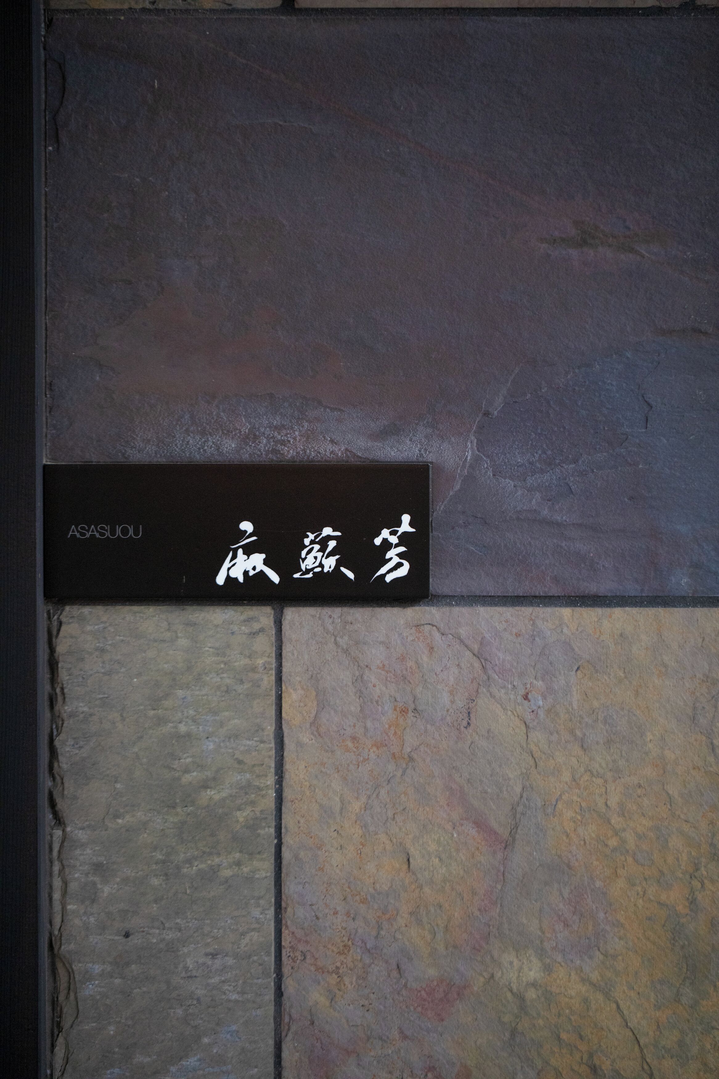 Un cartel con caracteres japoneses y el nombre 'ASASUOU' en una pared de piedra.