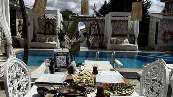 A poolside dining setup with a table, chairs, and a variety of food and drinks.