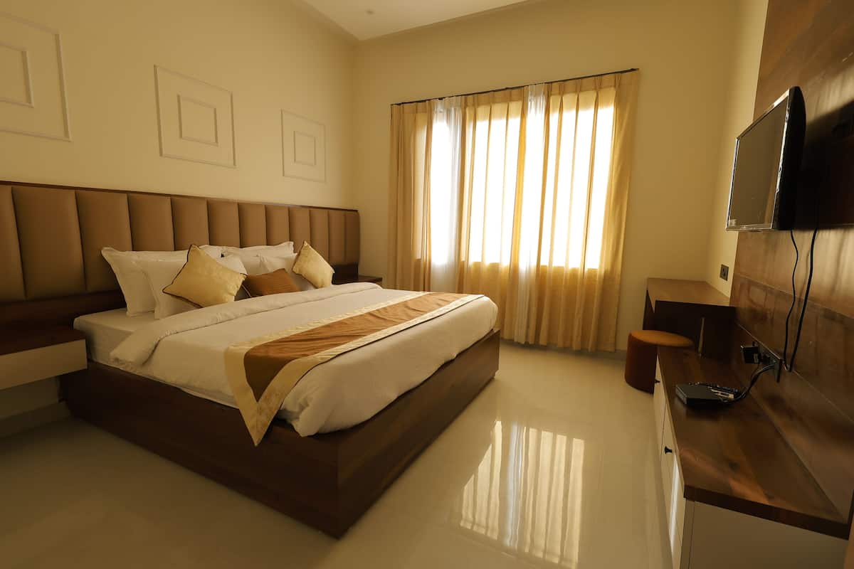 A modern hotel room with a large bed, a flat-screen TV mounted on the wall, and a wooden desk.
